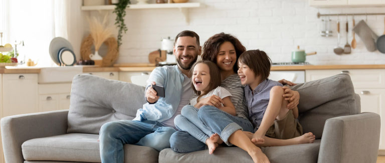 família sorrindo e se divertindo num sofá com a tranquilidade do seguro imobiliário
